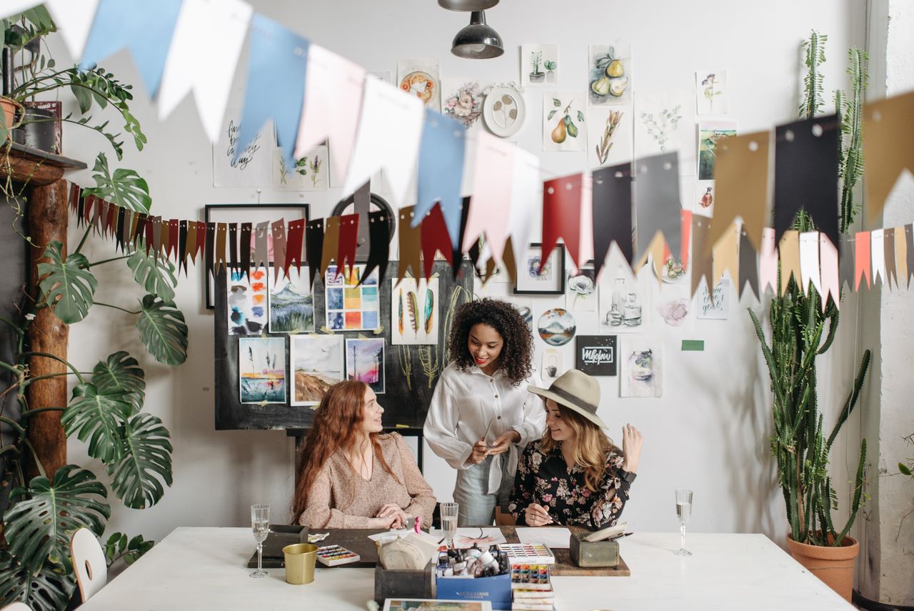 our-story Three women enjoying a creative painting session with colorful decor and plants.