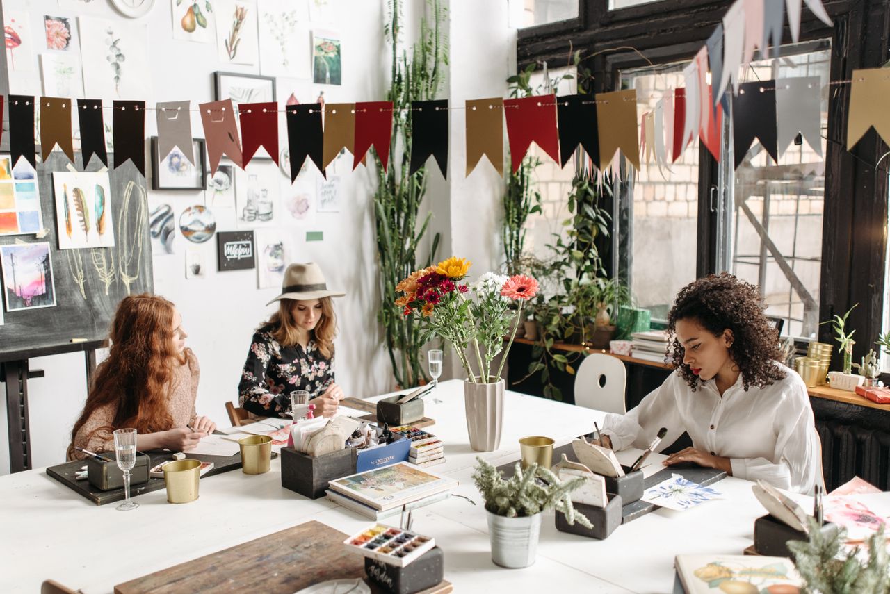 Three women engaged in a creative workshop, painting and drawing in a well-decorated studio space.